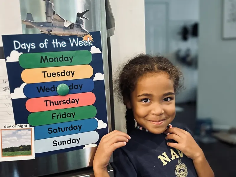Student holding a printed Days of the Week chart on a refrigerator with magnets