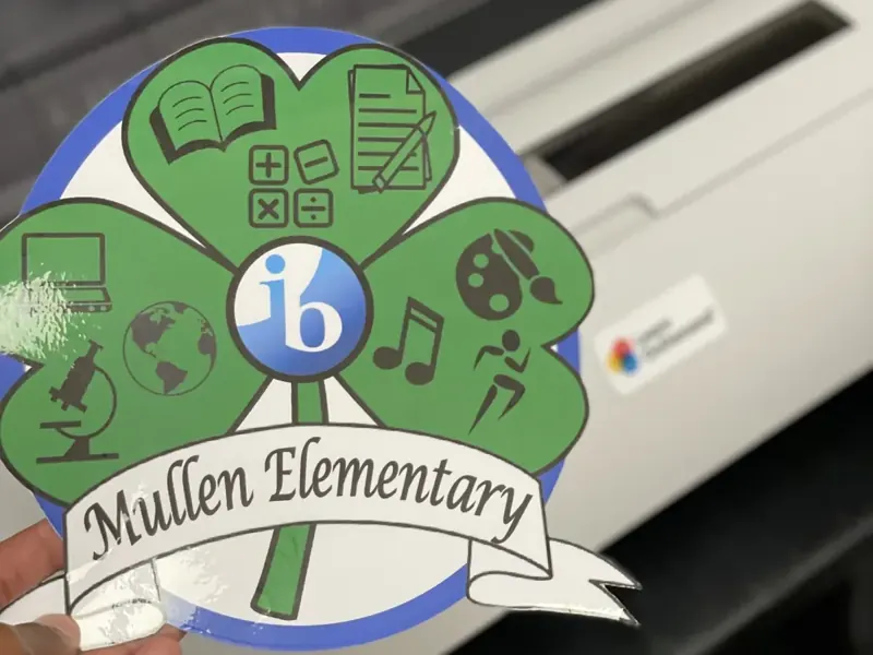Die-cut Mullen Elementary clover sticker held in front of a PSS Poster Maker